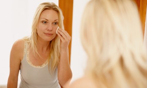 Face, mirror and girl with skincare cotton in bathroom for wellness, glowing skin or makeup removal in her home. Beauty, face or person with facial swab for toner, cleaning or product application.